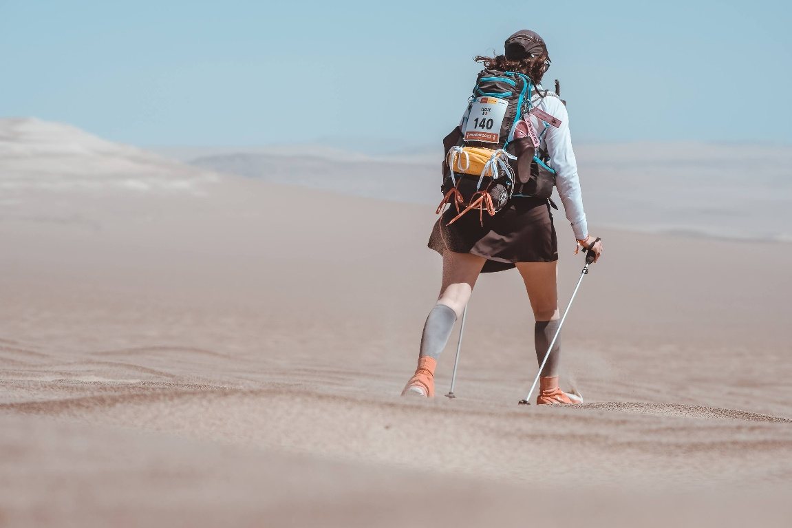 Cécile à l’arrivée d’une course dans le désert, médaille autour du cou, tentes et dunes derrière.